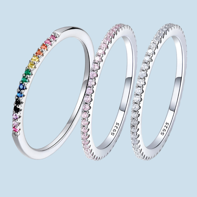 Three rings with multicolored gemstone inlays, displayed in a stacked arrangement, with the top ring featuring a rainbow-colored band, and the bottom two rings having a silver finish.