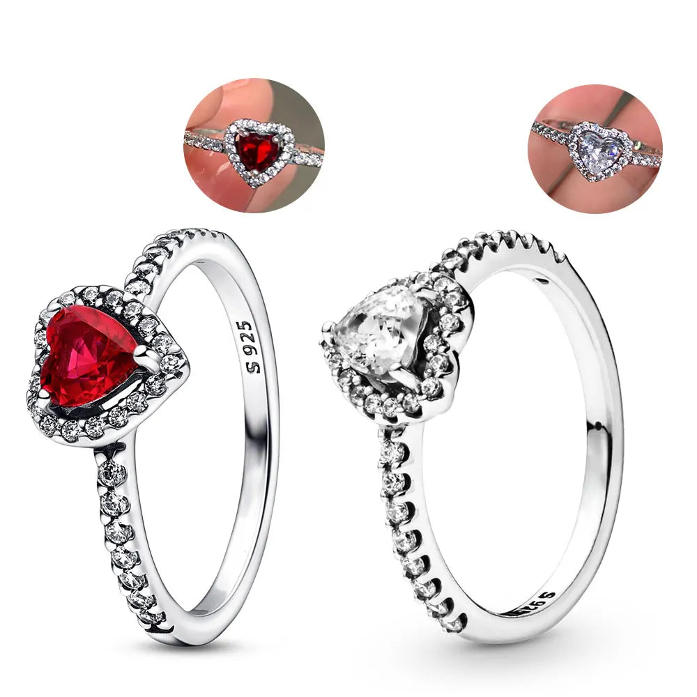 Two heart-shaped rings, one with a red zircon main stone and the other with a clear zircon main stone, both with silver bands and heart-shaped side stones.