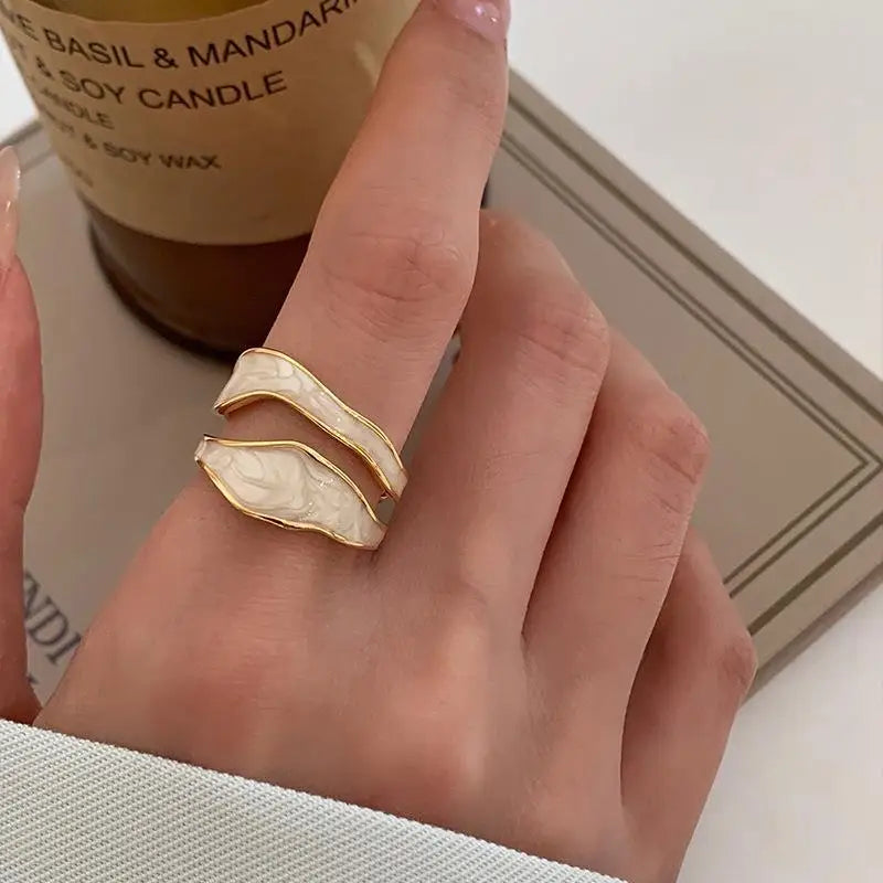 A person's hand wearing a white and gold geometric patterned ring.
