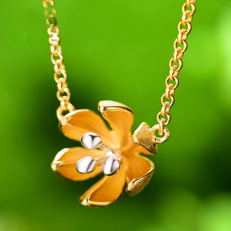 Gold plated silver cherry blossom flower necklace with a delicate two-tone floral pendant featuring gold petals and polished silver accents on a fine chain against a soft green background.