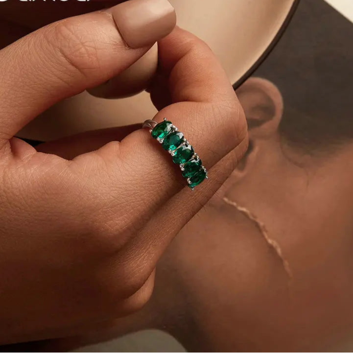 Close-up of a hand wearing a green gemstone ring with a blurred background