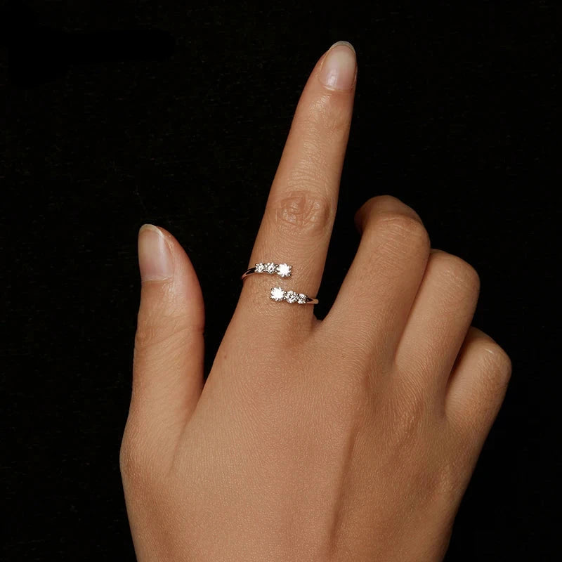 Hand wearing two silver rings with a clear gemstone on a black background,
