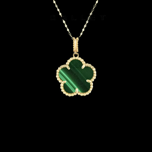 A gold necklace with a green clover-shaped pendant, displayed against a black background.