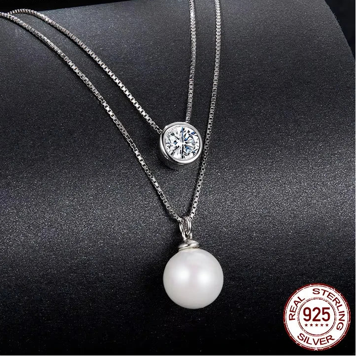 elegant piece of jewelry Double‑layer REAL 925 sterling silver necklace with a moissanite crystal pendant on the top chain and a white pearl drop on the lower chain, white gold‑plated finish, displayed on a dark textured background.